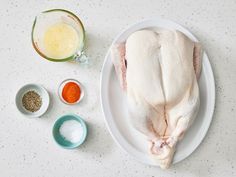 a whole chicken sitting on top of a white plate next to spices and seasonings