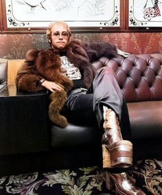 a man sitting on top of a leather couch in front of a wall with pictures