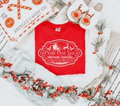 Step into the holiday spirit with our Candy Cane Christmas Shirt, featuring a charming Santa and reindeer design with the words "Candy Cane Lane Traditional Christmas Sweets & Treats" on a cozy Comfort Colors shirt. This Tis the Season tee is perfect for spreading holiday cheer, making it an essential for festive gatherings, tree farm outings, or Christmas parties. Whether you're looking for cute Christmas crewneck shirts or a candy cane T-shirt, this festive top blends classic holiday vibes wit Peppermint Christmas Shirt, Traditional Christmas Sweets, Candy Cane Shirts For Kids, Candy Cane T Shirt, Christmas Cotton T-shirt With Text Print, Candy Cane Sublimation, Candy Cane Lane, Xmas Tees, Candy Cane Christmas