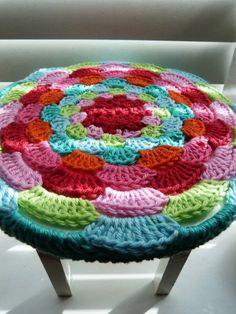 a multicolored crocheted stool sits on a white surface in front of a window