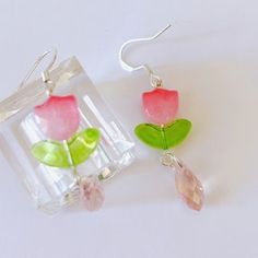 two flower shaped glass earrings with green leaves and pink flowers in the center, sitting on a white surface