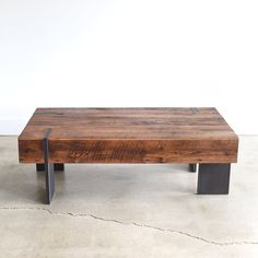 a wooden coffee table with metal legs on concrete flooring in front of a white wall