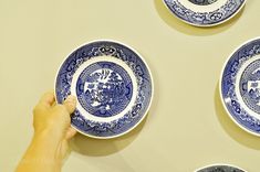 four blue and white plates being held up by someone's hand on the wall