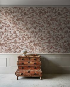 an old dresser in front of a wallpapered room with a vase on top