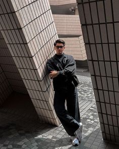 a man leaning against a wall with his arms crossed and looking at the camera while wearing sunglasses