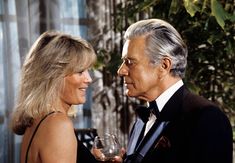 an older man and woman standing next to each other holding wine glasses in their hands