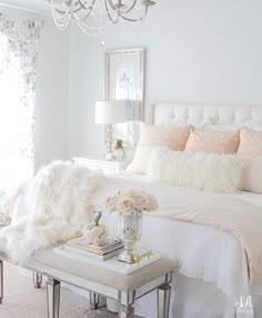 a white bedroom with a chandelier hanging from the ceiling and pillows on the bed