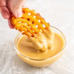 a person dipping some kind of food into a small glass bowl filled with mustard sauce