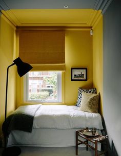 a bed sitting under a window next to a table with a lamp on top of it