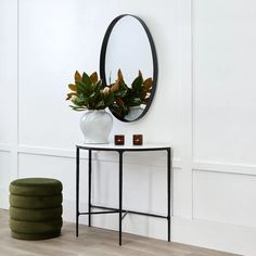 a white vase sitting on top of a table next to a mirror and green stool