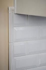 the corner of a kitchen with white tile on the wall and cupboards behind it