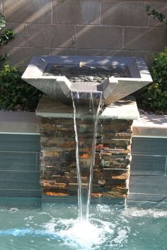 an outdoor fountain with water running from it's sides into the pool and surrounded by rocks