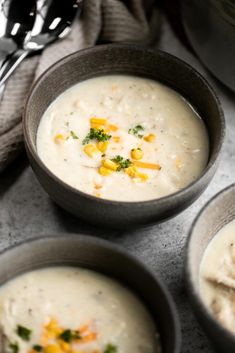 three bowls filled with soup and garnished with corn on the top, next to two silver spoons