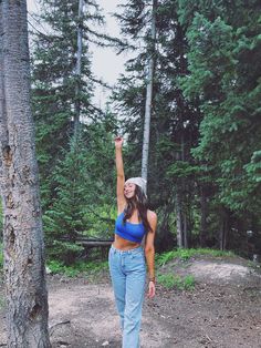 a woman standing in front of a tree reaching up into the air with her hand