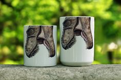 two coffee mugs with an image of a dinosaur on them