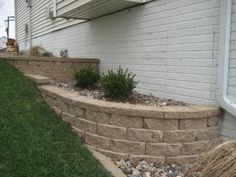 a stone wall next to a house with grass and rocks in the front yard area