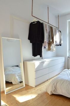 an empty bedroom with white furniture and clothes hanging on the rack in front of it