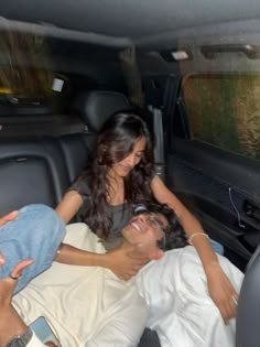 a man and woman laying in the back of a car