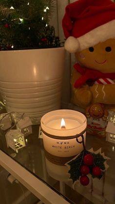 a lit candle sitting on top of a glass table next to a teddy bear and christmas decorations