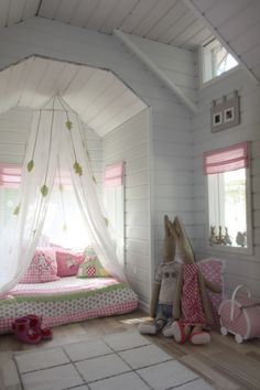 a bedroom with white walls and wooden floors has pink accents on the bed, along with two stuffed animals