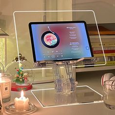 a computer monitor sitting on top of a desk next to a candle and some books