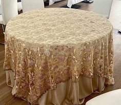 a round table covered with a beige and gold tablecloth on top of a hard wood floor