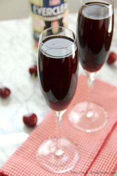 two glasses filled with liquid sitting on top of a red table cloth next to a bottle