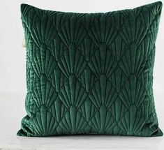 a green velvet pillow sitting on top of a white table