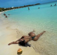 a woman laying on top of a sandy beach next to the ocean with people in the background