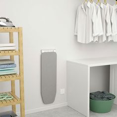 a white bathroom with clothes hanging on the rack and an ironing board next to it