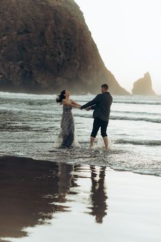 a man and woman are holding hands in the water at the beach near some cliffs