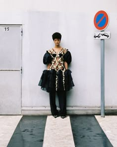 a woman standing in front of a white wall next to a street sign and crosswalk