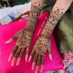 two hands with henna designs on them sitting next to each other in front of a pink pillow