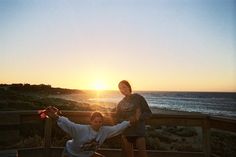 two women posing for the camera in front of an ocean view at sunset or sunrise