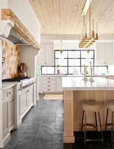 a large kitchen with white cabinets and wood ceilinging, along with two stools at the island