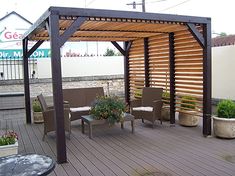 an outdoor covered patio area with chairs and plants on the deck, next to a hot tub