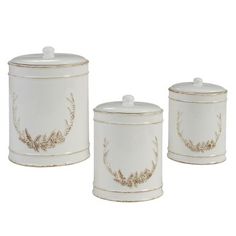 three white canisters with gold designs on the sides and one has a lid