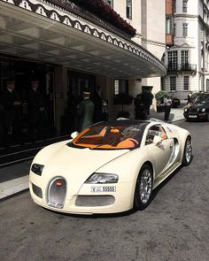 a white bugatti parked in front of a building with people walking by it