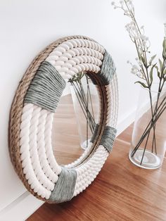 a vase with flowers in it next to a roped circular mirror on a wooden floor