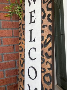 a welcome sign hanging from the side of a brick wall next to a door way