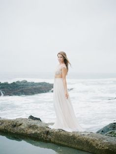 a woman in a white dress standing on rocks near the ocean