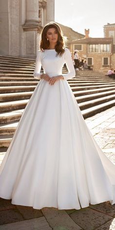 a woman in a white wedding dress standing on steps with her hands on her hips