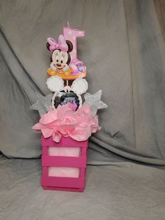 a minnie mouse 1st birthday cake in a pink box on a gray background with silver stars