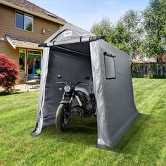 a motorcycle is parked in front of a tent on the grass next to a house