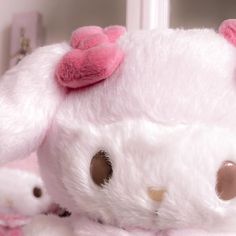 a white stuffed animal with a pink bow on it's head and ears, sitting next to other stuffed animals