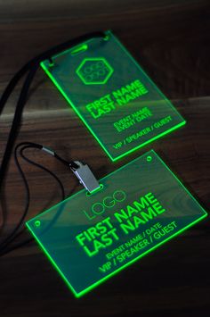 two name tags are glowing green on a wooden surface with a lanyard attached to it