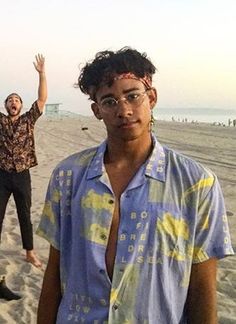 two men standing on the beach with their arms in the air and one holding his hand up