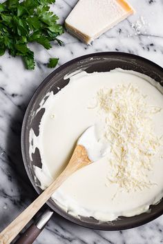 a pan filled with cheese and cream on top of a marble counter next to a wooden spoon