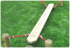 a wooden bench sitting on top of a green grass covered field next to a red rope