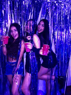 three women are posing for the camera in front of purple tinsel and streamers